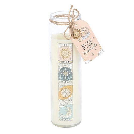 A tall glass jar candle filled with white wax, featuring a vertical decorative label with celestial and geometric motifs in muted blue, gold, and beige tones. A kraft twine bow and a peach-colored paper tag tied to the rim read 'ROSE' and 'Scented Candle.