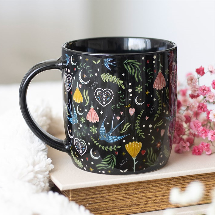 Black mug with colorful designs on a white surface with pink flowers