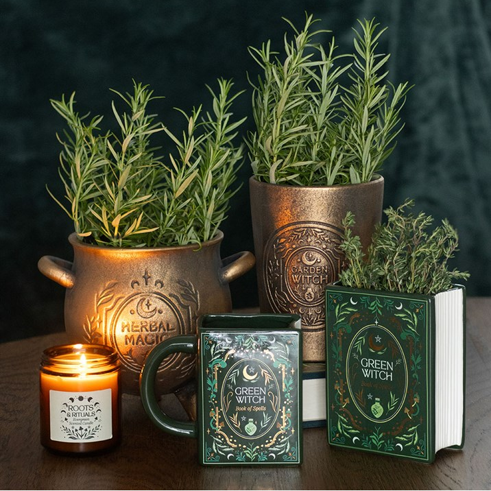 Decorative set with plants in copper pots, a candle, and a book titled 'Green Witch' on a dark background.