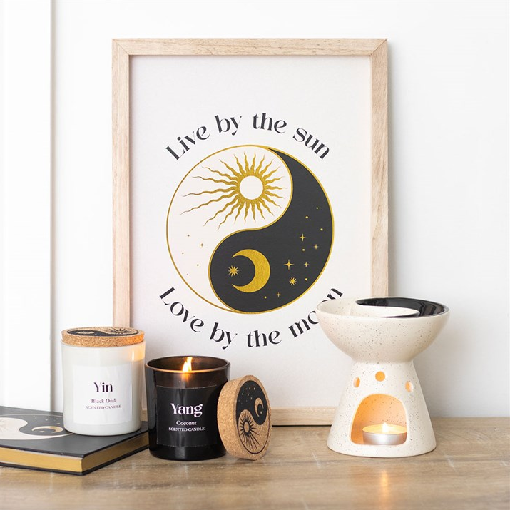 Framed artwork with sun and moon design on a table with candles and decor items.