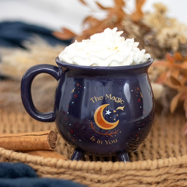 Navy mug with 'The Magic is in You' text and moon design, filled with whipped cream, on a textured surface.