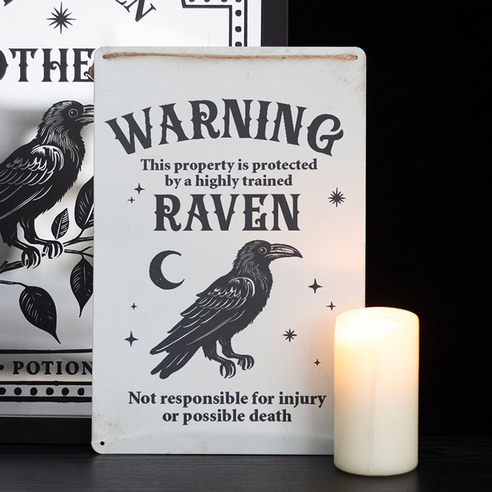 Decorative sign with a raven design and text, placed next to a candle on a dark surface.