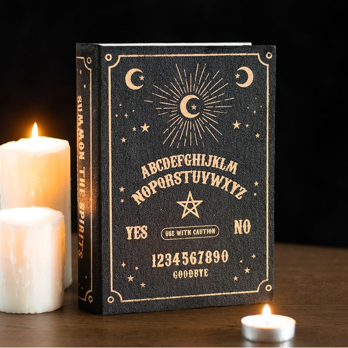Decorative book with Ouija board design on a wooden surface with candles.