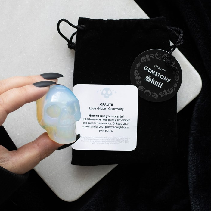 Opalite crystal skull held by a hand with a branded drawstring bag in the background