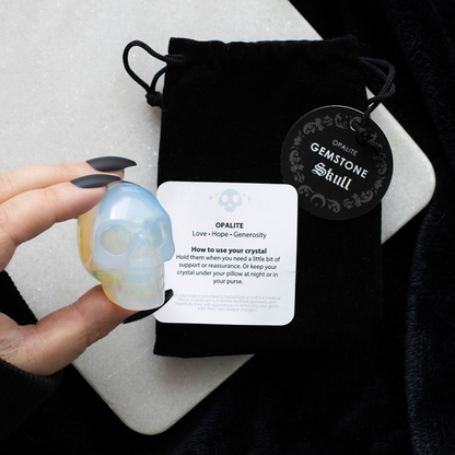 Opalite crystal skull held by a hand with a branded drawstring bag in the background
