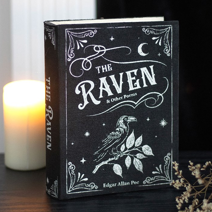 Book titled 'The Raven' by Edgar Allan Poe with decorative cover design, placed on a surface with a candle and flowers in the background.