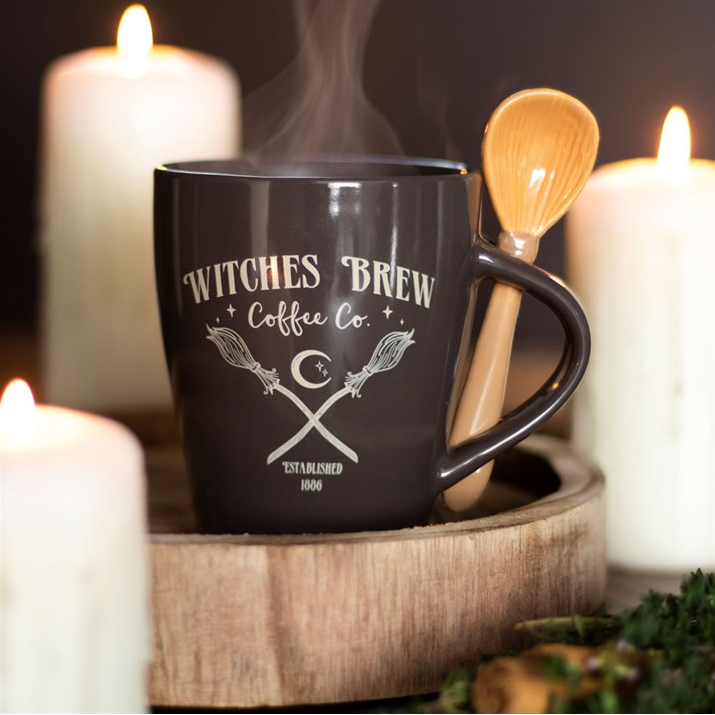 Black mug with 'Witches Brew Coffee Co.' text and design, surrounded by candles and a wooden spoon.