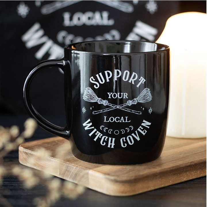Black mug with 'Support Your Local Witch Coven' text on a wooden coaster.