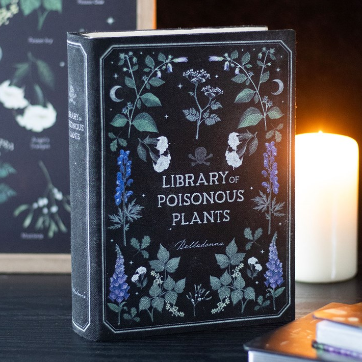 Book titled 'Library of Poisonous Plants' with decorative cover featuring plants and text, on a dark surface with a candle in the background.