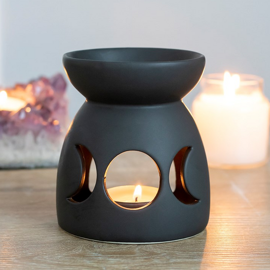 Black ceramic oil burner with cut-out moon phases on a wooden surface.