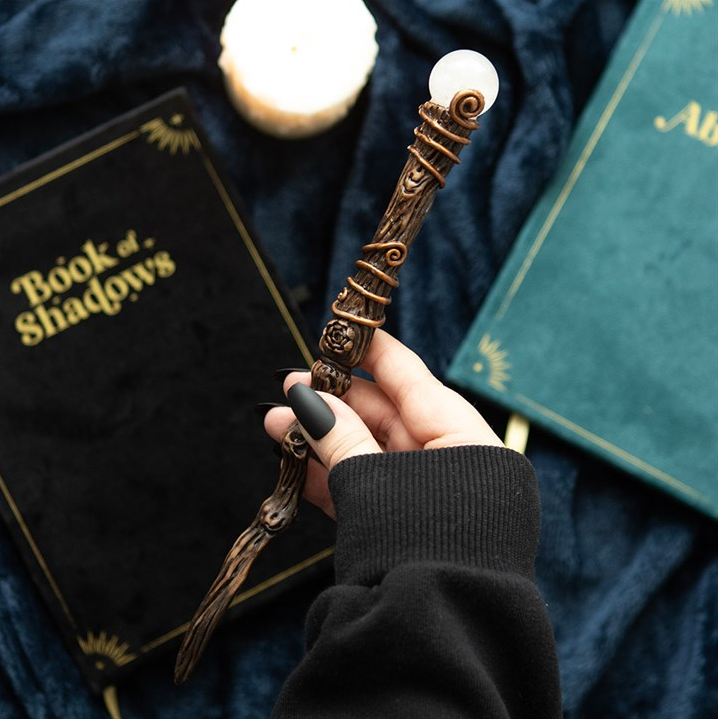 Hand holding a decorative object with 'Book of Shadows' and 'Albus' on books in the background