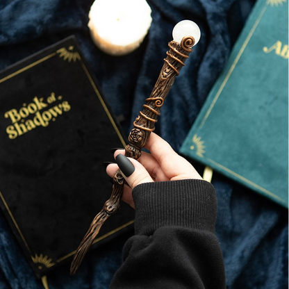 Hand holding a decorative object with 'Book of Shadows' and 'Albus' on books in the background