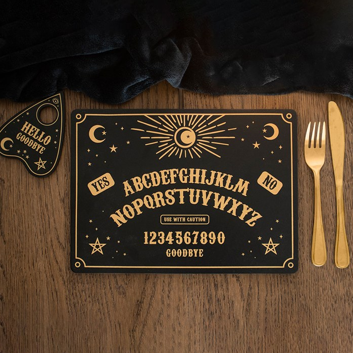 Decorative Ouija board on a wooden surface with gold cutlery.