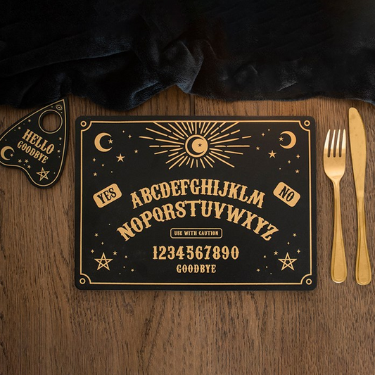 Decorative Ouija board on a wooden surface with gold cutlery.
