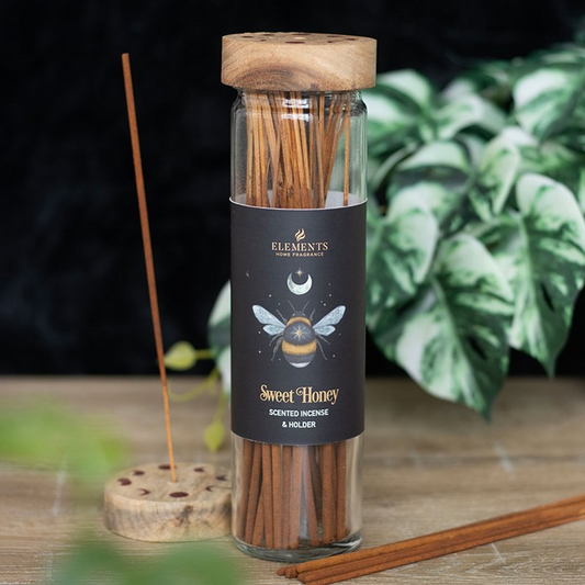 Incense sticks in a glass bottle with wooden cap on a wooden surface, surrounded by green leaves.