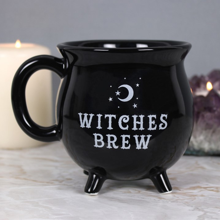 Black mug with 'Witches Brew' text on a marble surface with candles in the background