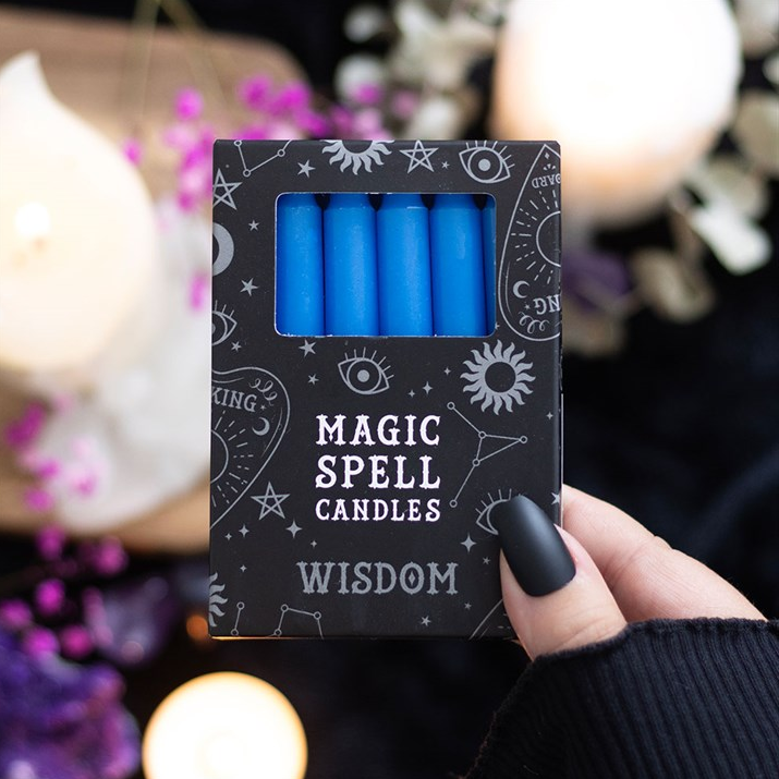 Pack of blue candles labeled 'Magic Spell Candles Wisdom' held by a hand with a blurred candlelit background.