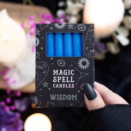 Pack of blue candles labeled 'Magic Spell Candles Wisdom' held by a hand with a blurred candlelit background.