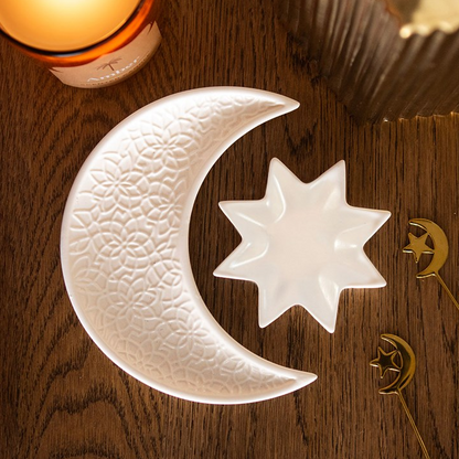 Decorative ceramic moon and star dish on a wooden surface with a candle in the background.