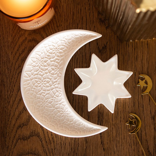 Decorative ceramic moon and star dish on a wooden surface with a candle in the background.