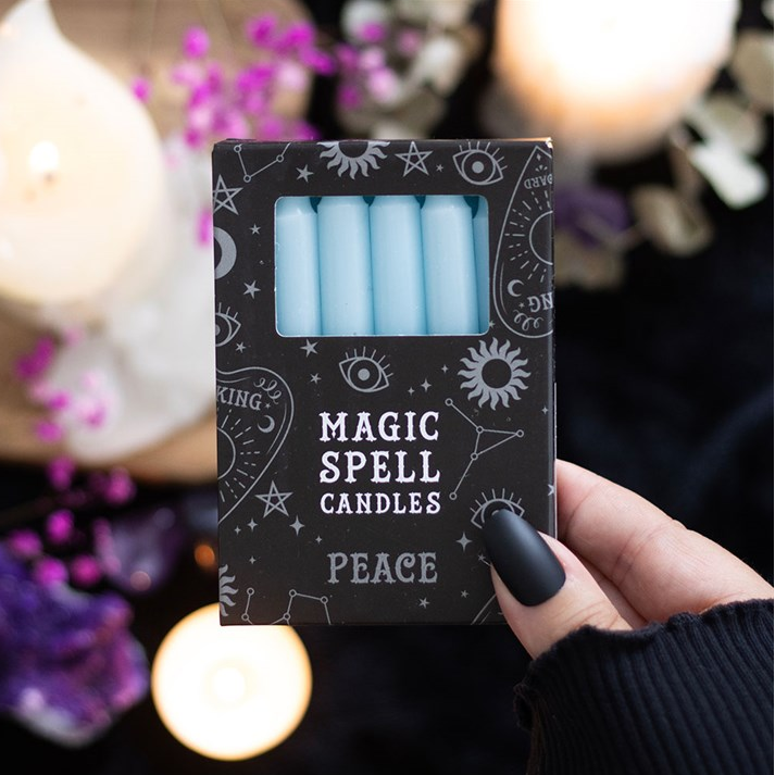 Pack of 'Magic Spell Candles' labeled 'Peace' held by a hand with blurred candles and flowers in the background.