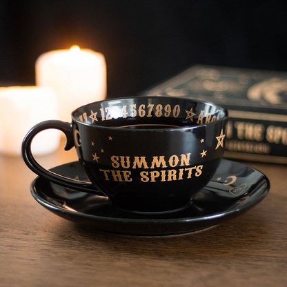 Black cup and saucer set with 'Summon the Spirits' text on a wooden surface with candles in the background.