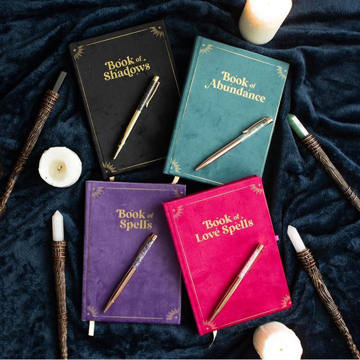 Four themed journals with pens on a dark fabric background
