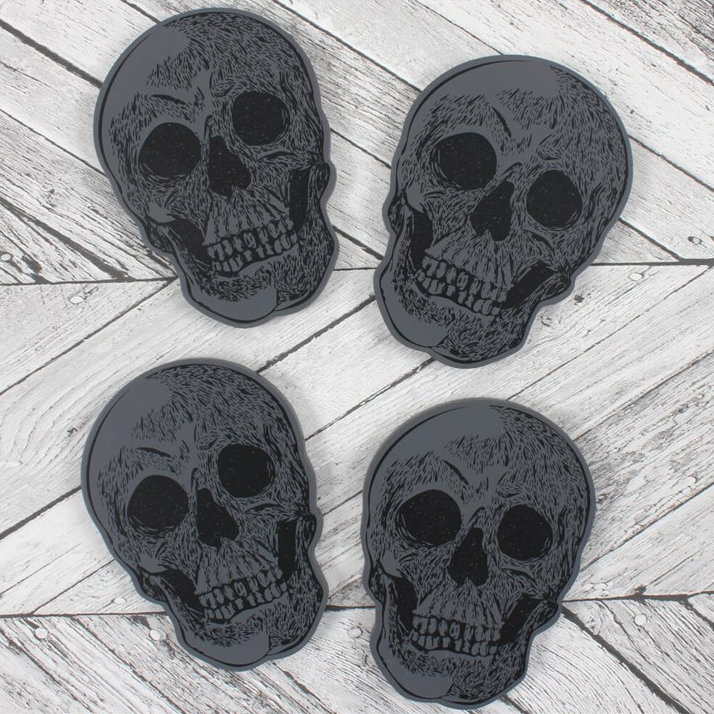 Four black skull-shaped coasters on a wooden surface