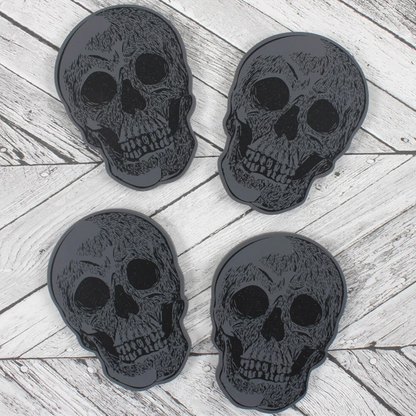 Four black skull-shaped coasters on a wooden surface