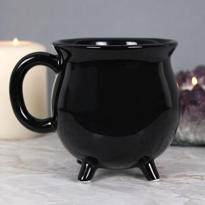Black ceramic mug with legs on a marble surface with candles in the background