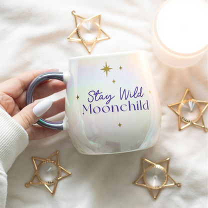 Mug with 'Stay Wild Moonchild' text held by a hand, surrounded by decorative star-shaped objects on a white background.