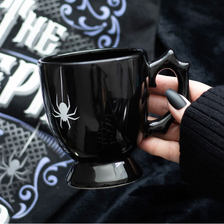 Black mug with spider design held by a hand against a dark background
