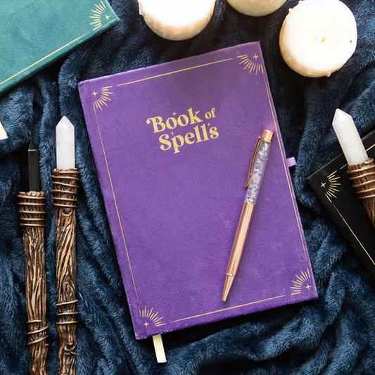 Purple notebook titled 'Book of Spells' with candles and wands on a dark fabric background