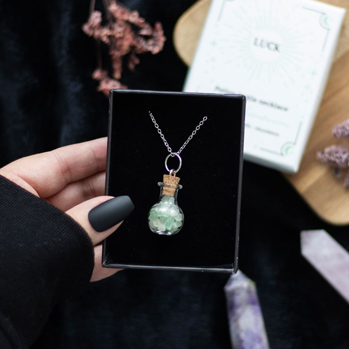 Hand holding a necklace with a green pendant in a black box, with a blurred background.