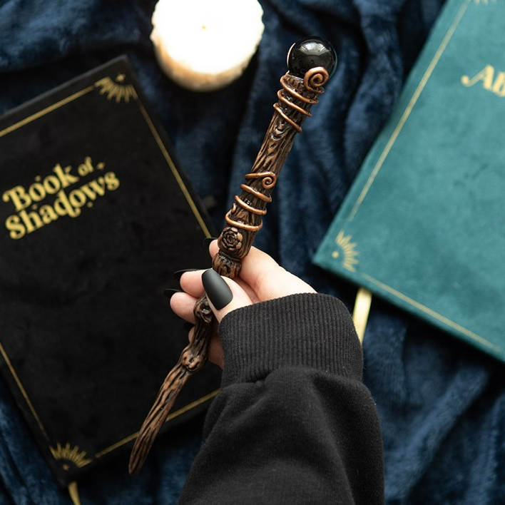 Hand holding a decorative wand over books titled 'Book of Shadows' and 'Albus'.