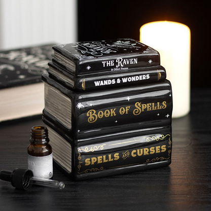 Stack of books titled 'Book of Spells', 'Wands & Wonders', and 'Spells & Curses' on a dark surface with a candle in the background.