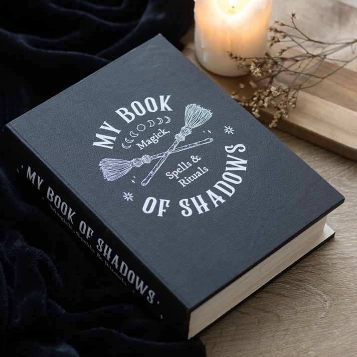 Black book titled 'My Book of Shadows' with a decorative cover on a wooden surface.