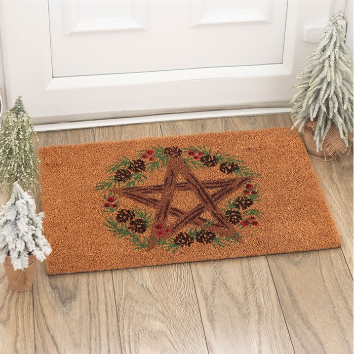 Doormat with pentacle design on a wooden floor in front of a white door.