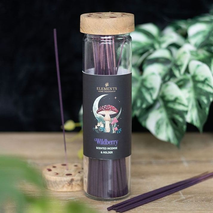 Incense sticks in a glass bottle with a wooden cap on a wooden surface, surrounded by greenery.