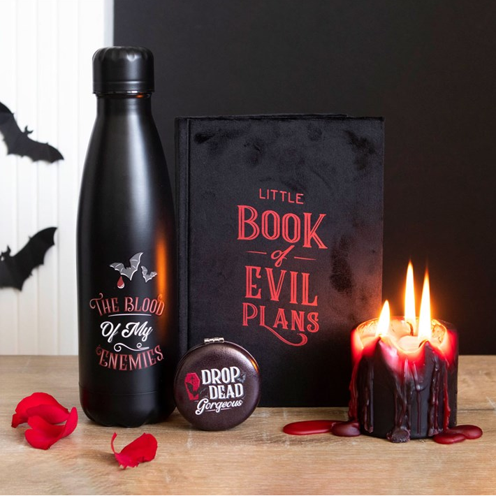 Black water bottle, 'Little Book of Evil Plans', and candles on a wooden surface with bats in the background.