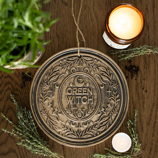 Decorative circular sign with 'Green Witch' text on a wooden surface with candles and plants.