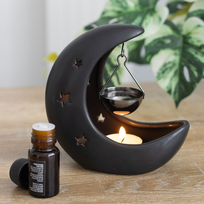 Black moon-shaped candle holder with a lit candle and a small bottle on a wooden surface.
