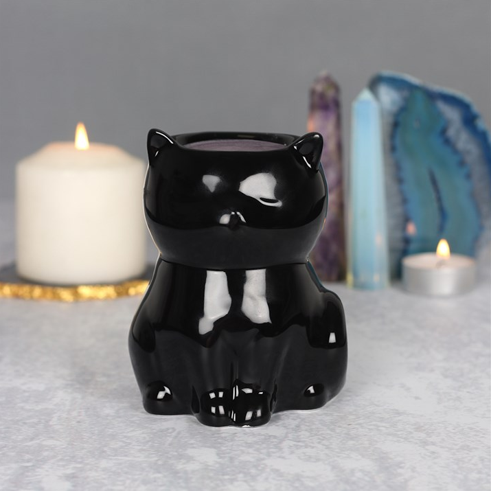 Black cat-shaped candle holder on a gray surface with candles and crystals in the background.