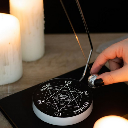 Hand using a dowsing rod on a black crystal grid with candles in the background