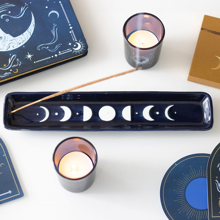 Candle holders with moon phases and incense on a white surface