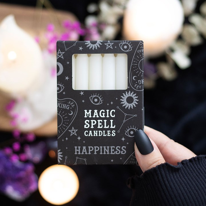 Box of 'Magic Spell Candles Happiness' with candles inside, held by a hand against a blurred candlelit background.