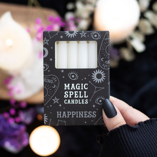 Box of 'Magic Spell Candles Happiness' with candles inside, held by a hand against a blurred candlelit background.