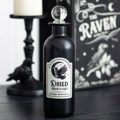 Black bottle labeled 'Dried Crow's Feet' with decorative background featuring a candle and 'The Raven' book.
