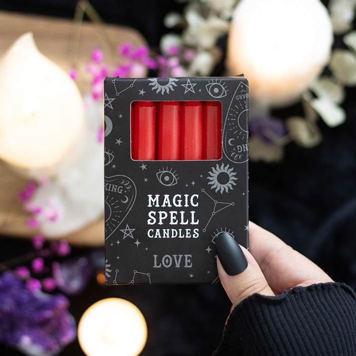 Box of 'Magic Spell Candles' with red candles inside, held by a hand against a mystical background.