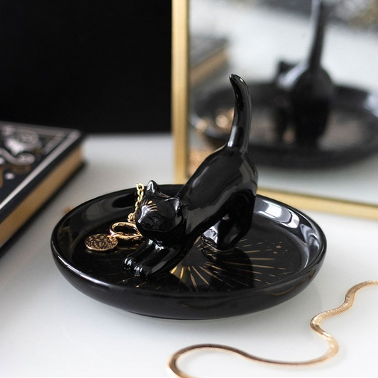 Black cat-shaped jewelry dish on a white surface with a mirror in the background